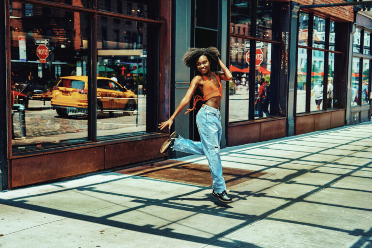 female urban dancer jumping outdoors on sidewalk in front of store.