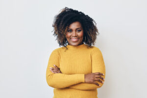 Portrait of smiling beautiful Afro woman standing with arms crossed. Yellow sweater