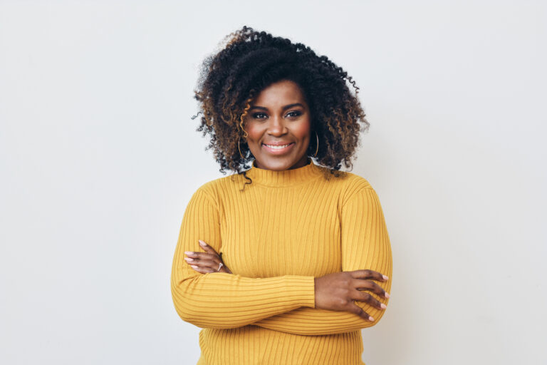 Portrait of smiling beautiful Afro woman standing with arms crossed. Yellow sweater